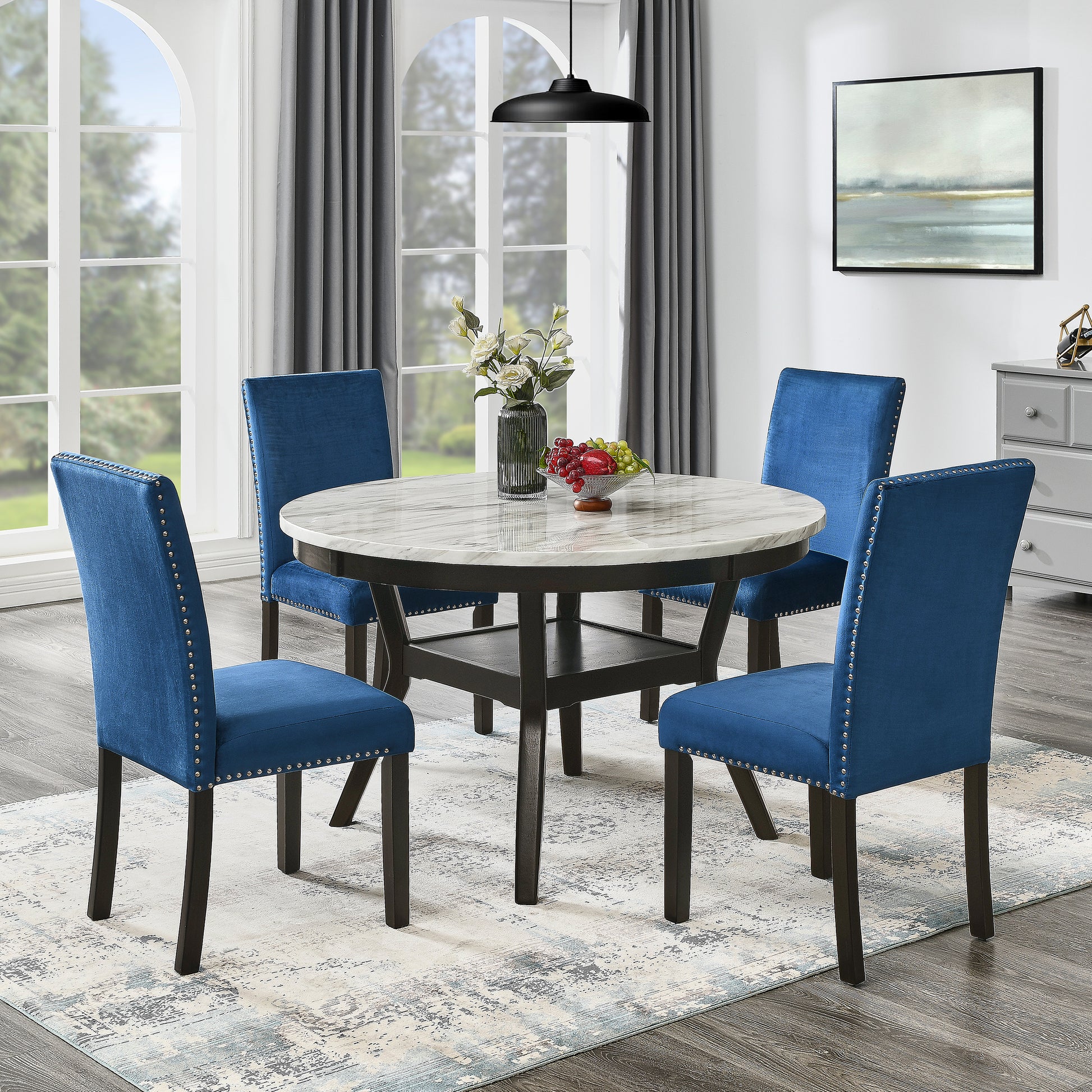 Round marble top dining table with dark wood base and four blue velvet dining chairs with silver nailhead trim