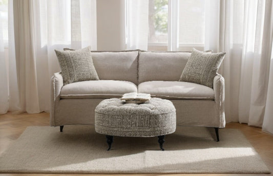 Light grey upholstered sofa with patterned throw pillows central oval ottoman with tufted geometric design