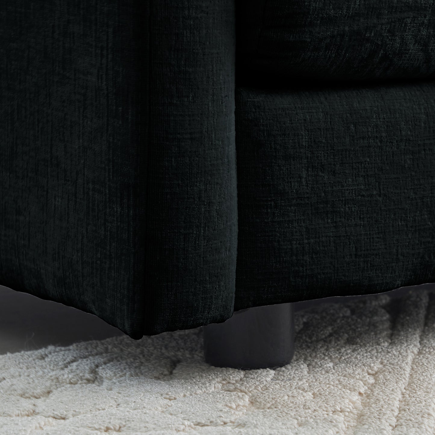 Closeup of dark charcoal textured fabric sofa armrest and black cylindrical leg