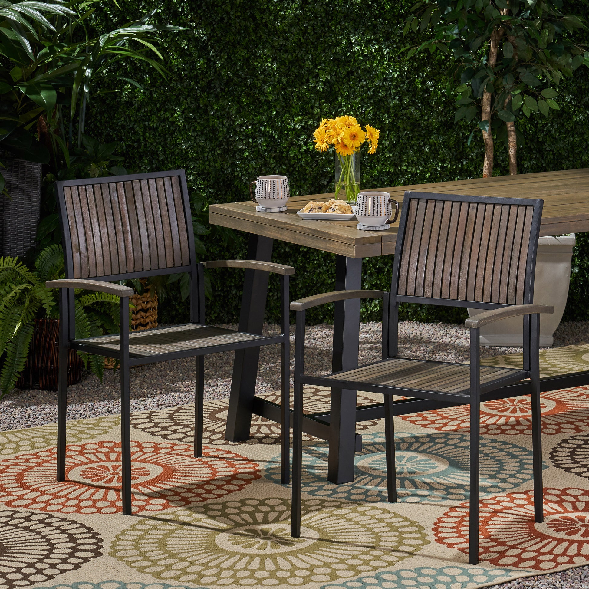 Two modern outdoor dining chairs with dark wood slats and black metal frames on a patterned rug