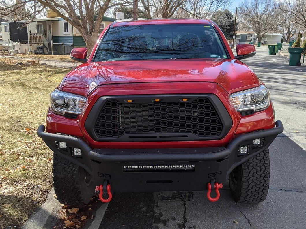 Red Toyota Tacoma truck with black mesh grille and aftermarket bumper