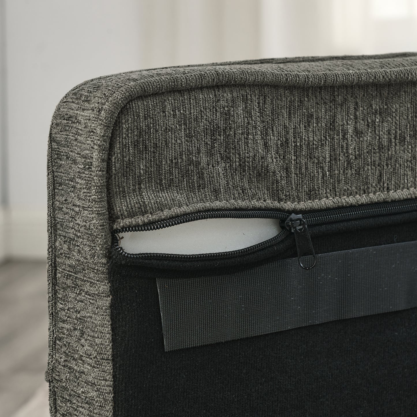 Closeup of a dark grey fabric armchair showing its zippered underside and foam padding