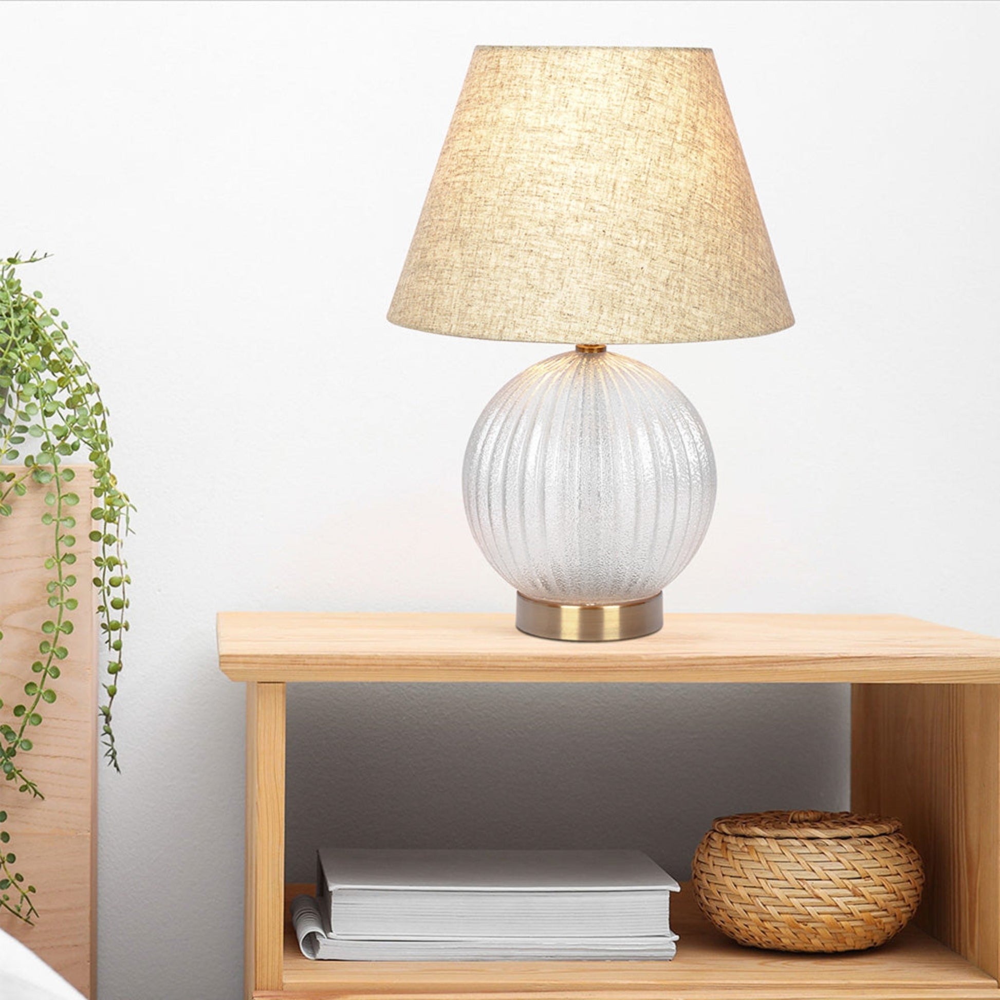 Glass fluted table lamp with linen shade on wooden nightstand