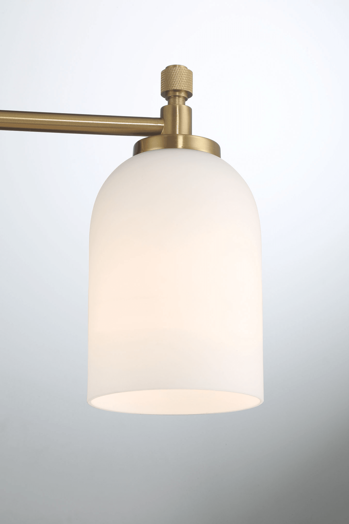 Closeup of a modern brass desk lamp with a frosted glass shade and adjustable arm