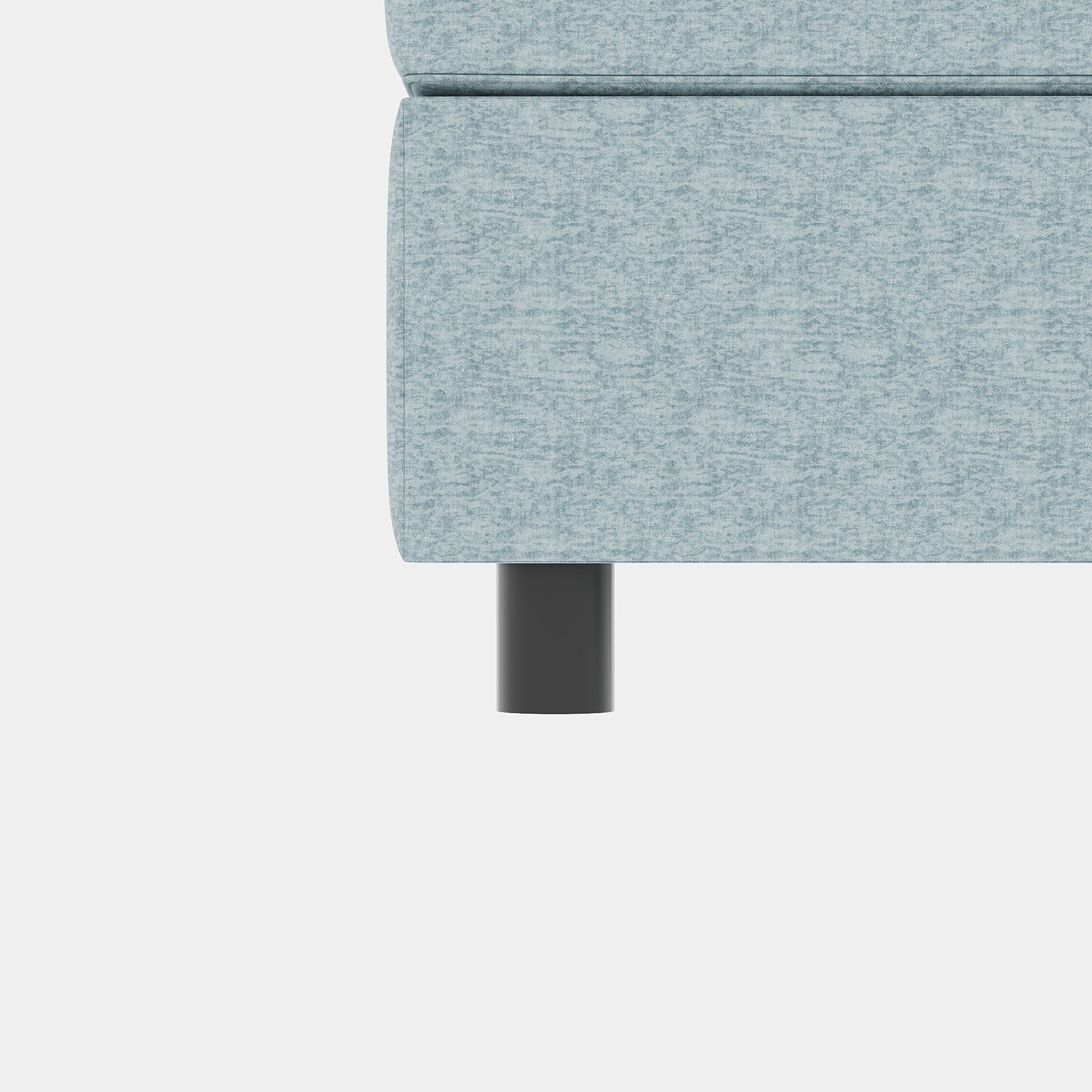 Close up of a light blue textured fabric on a sofa arm with a dark grey cylindrical leg
