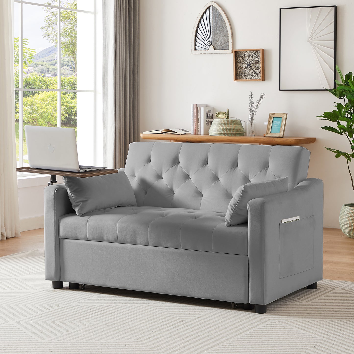 Grey upholstered sofa bed with diamond tufting and attached side tray holding a laptop