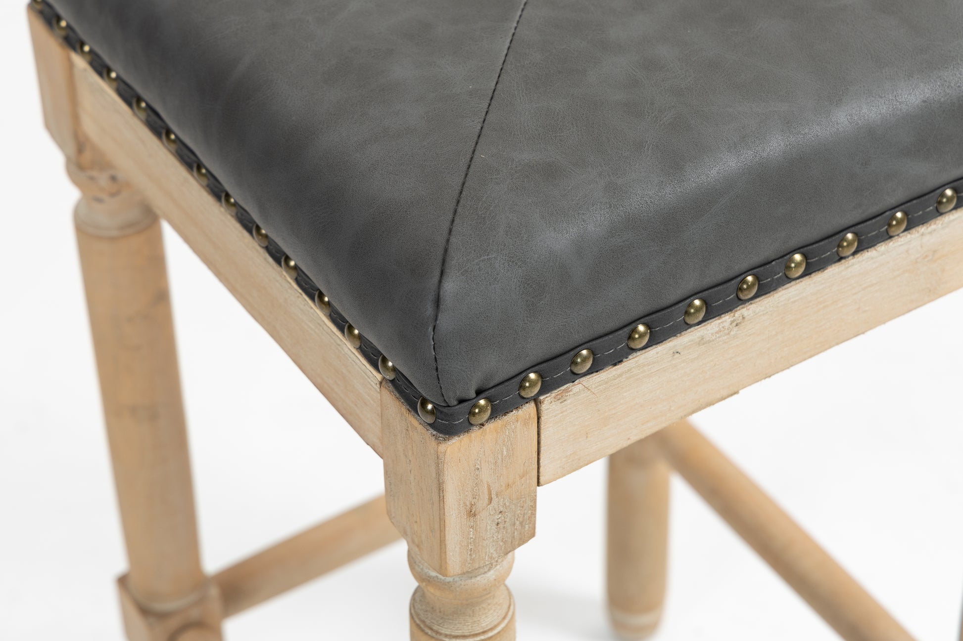 Closeup of a dark grey faux leather seat with brass stud accents on a distressed wood frame