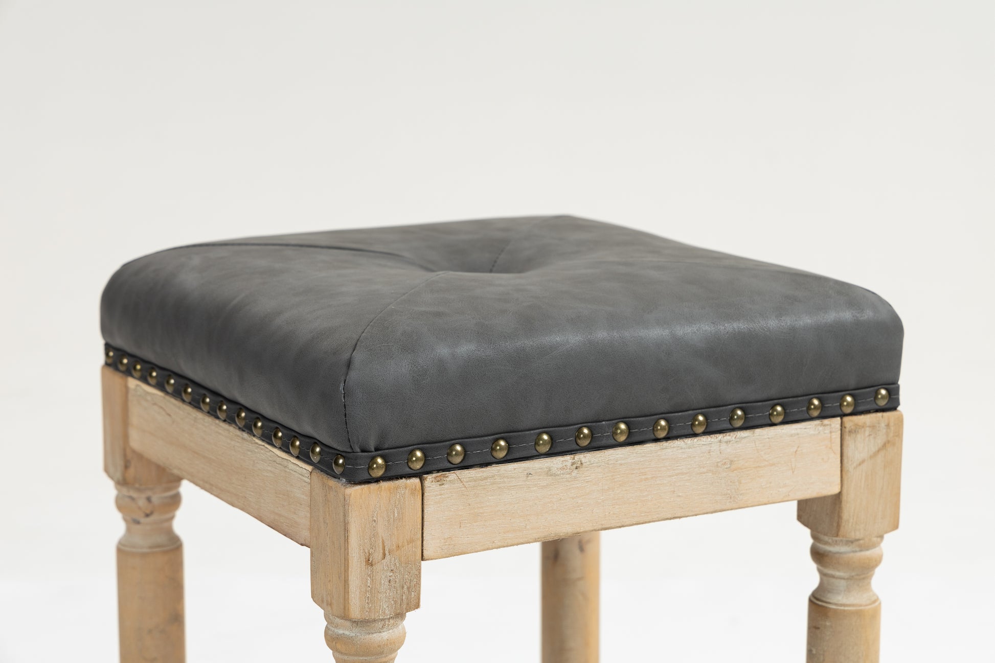 Dark gray tufted faux leather stool with nailhead trim and distressed wood legs