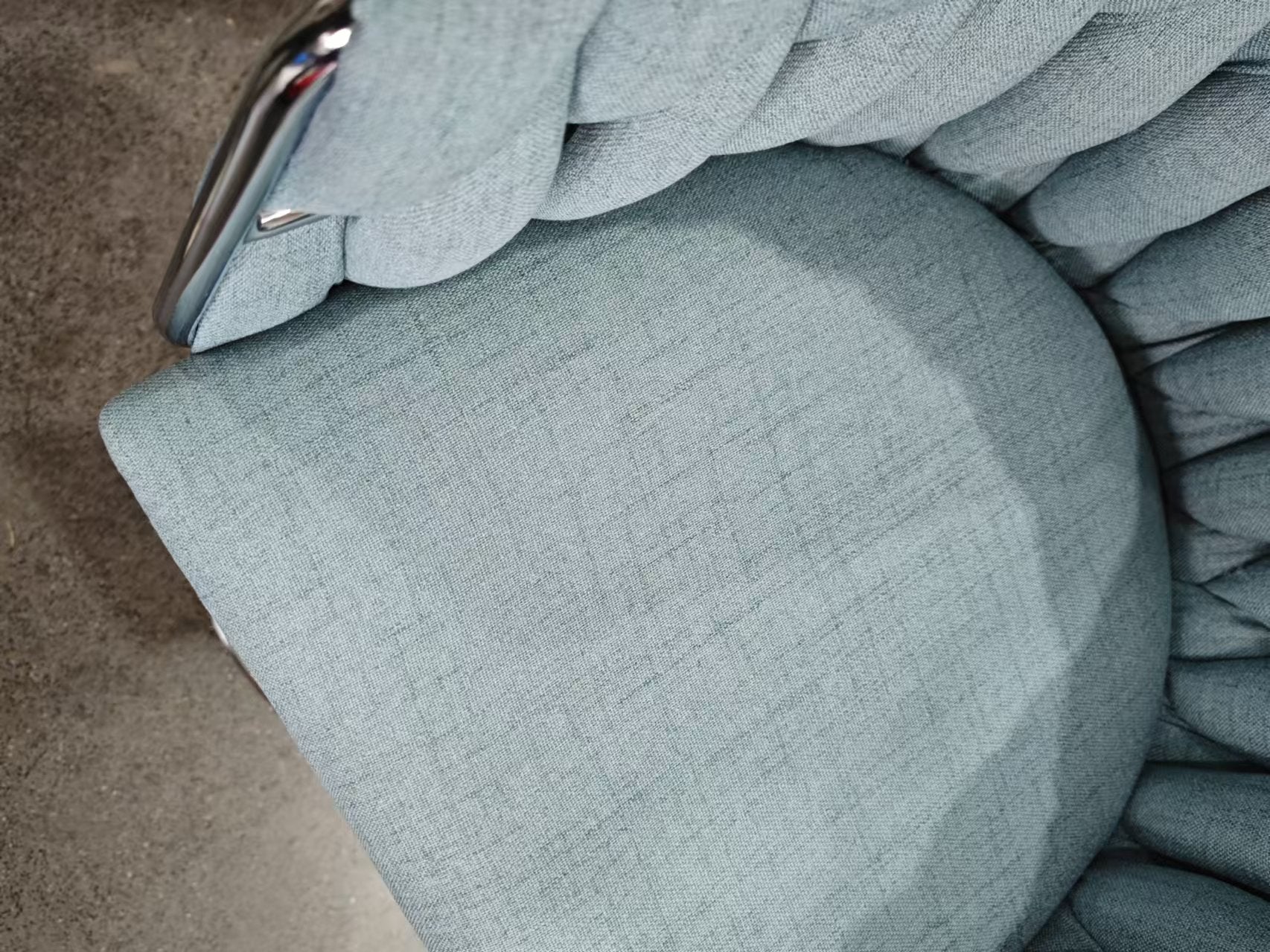 Closeup of a textured blue fabric armchair cushion with chrome armrest detail