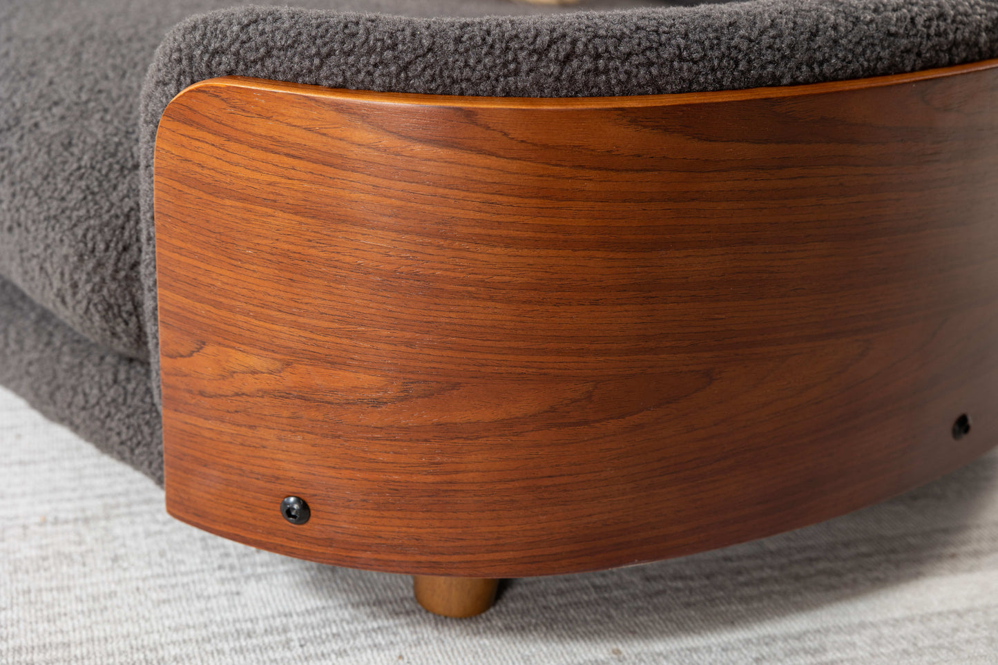 Curved dark wood panel accenting a grey boucle armchair showcasing texture