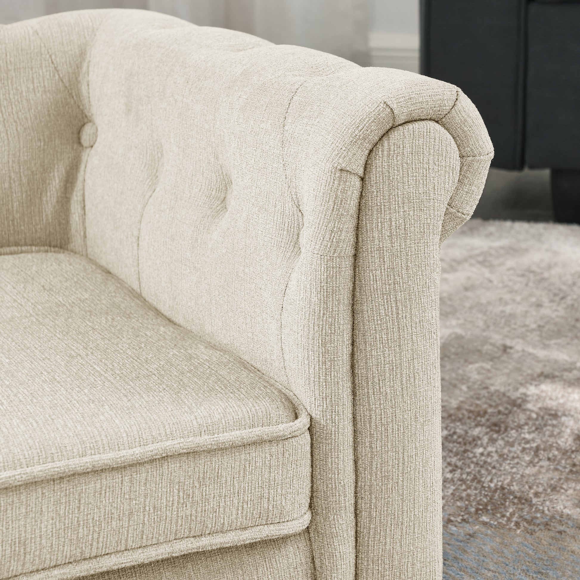 Closeup of a tufted beige fabric armchair armrest with textured weave showcasing classic design elements