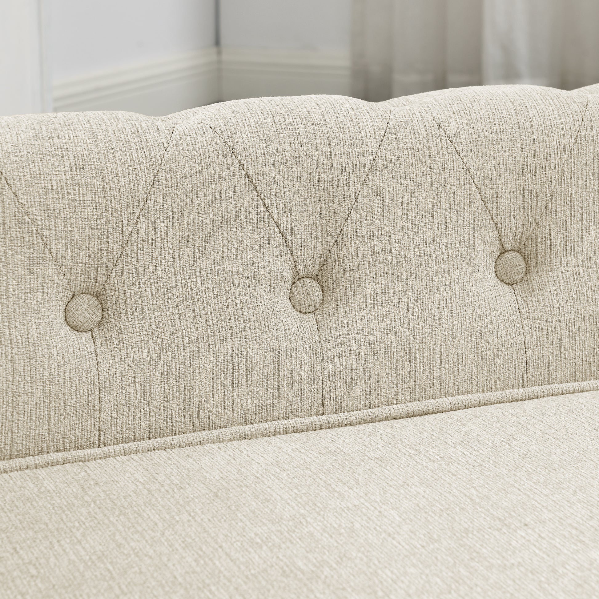 Closeup of beige linen upholstered sofa with button tufting on the backrest