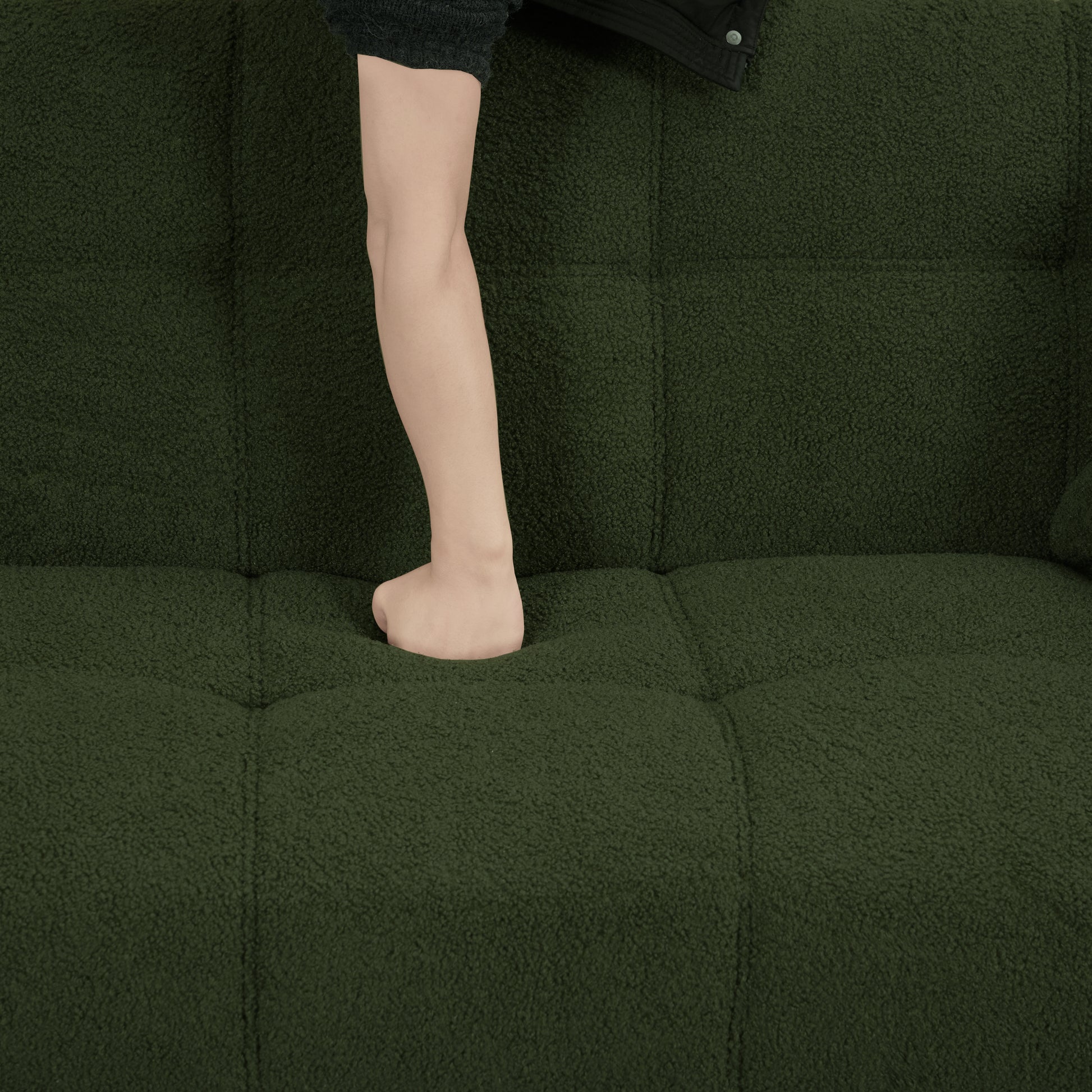 Deep green teddy fabric sofa with tufted seat and a childs leg pressing into cushion