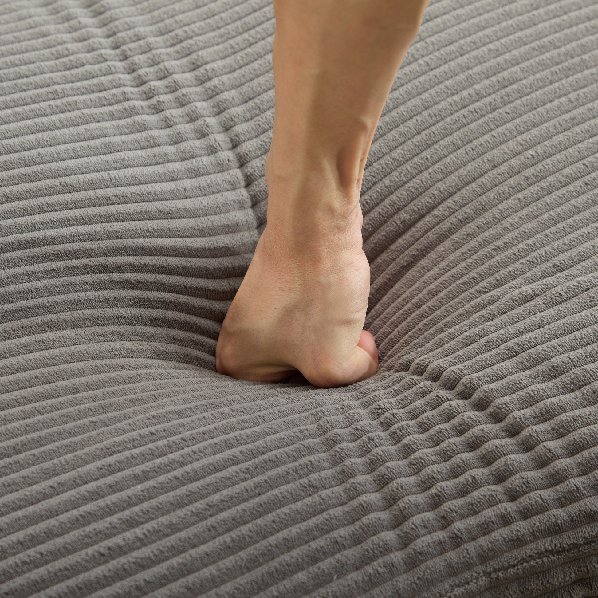 Foot pressing into plush gray corduroy fabric highlighting its softness