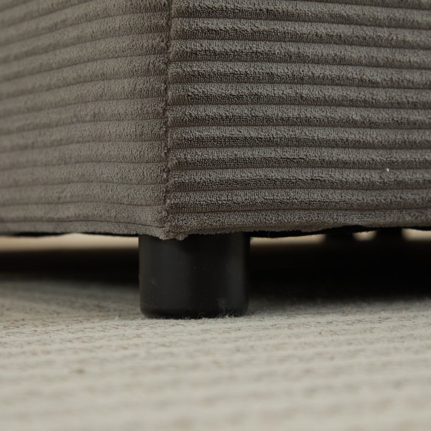 Closeup of grey corduroy fabric on a sofa base with black legs