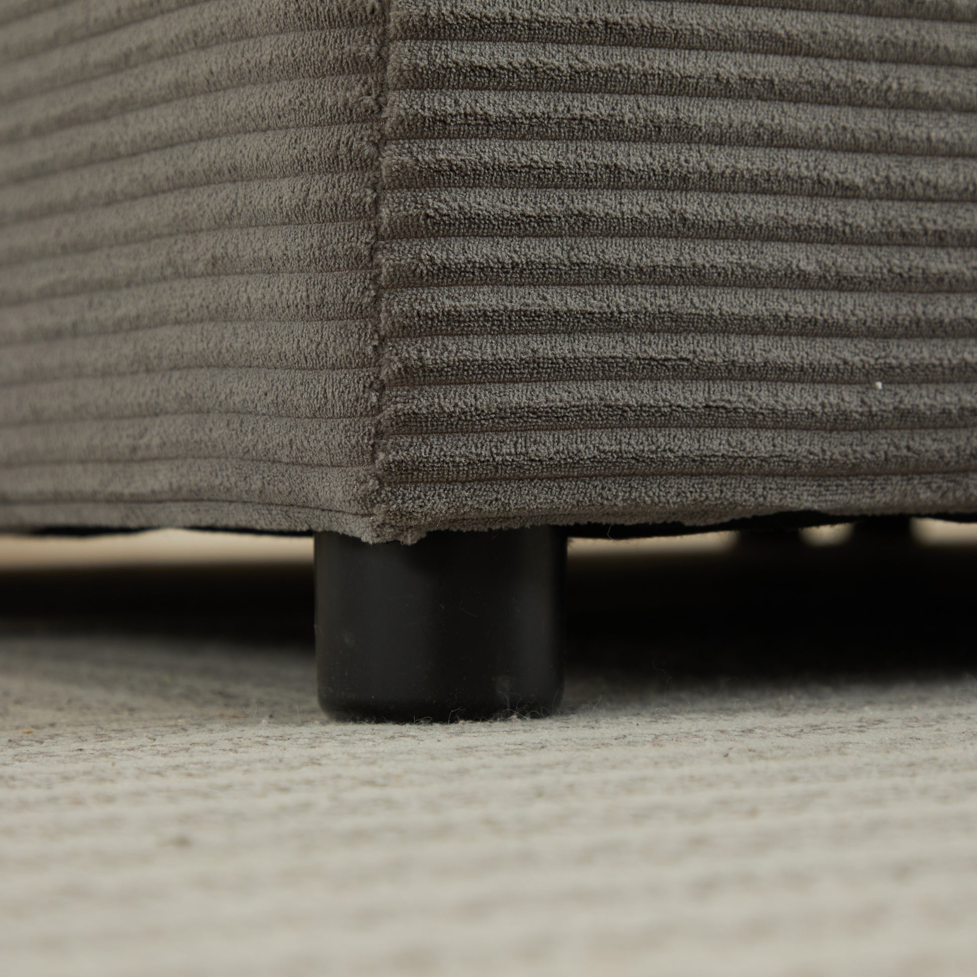 Closeup of grey corduroy fabric on a sofa base with black legs