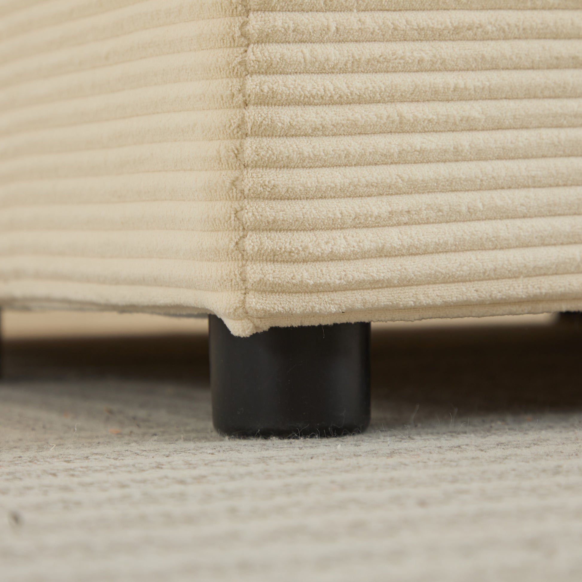 Closeup of a cream corduroy fabric ottoman base with black cylindrical legs