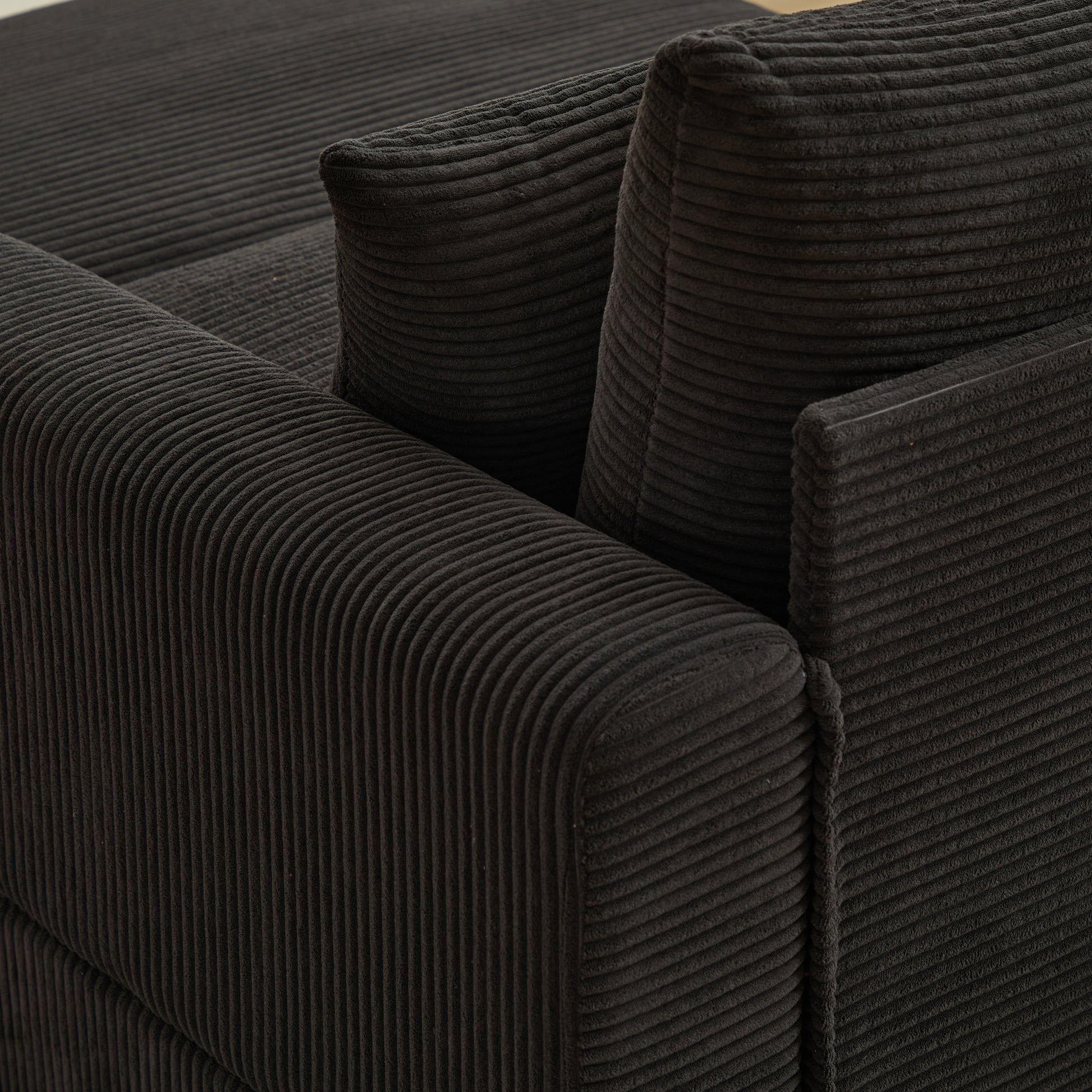 Closeup of a charcoal grey corduroy sofa armrest with plush cushioning