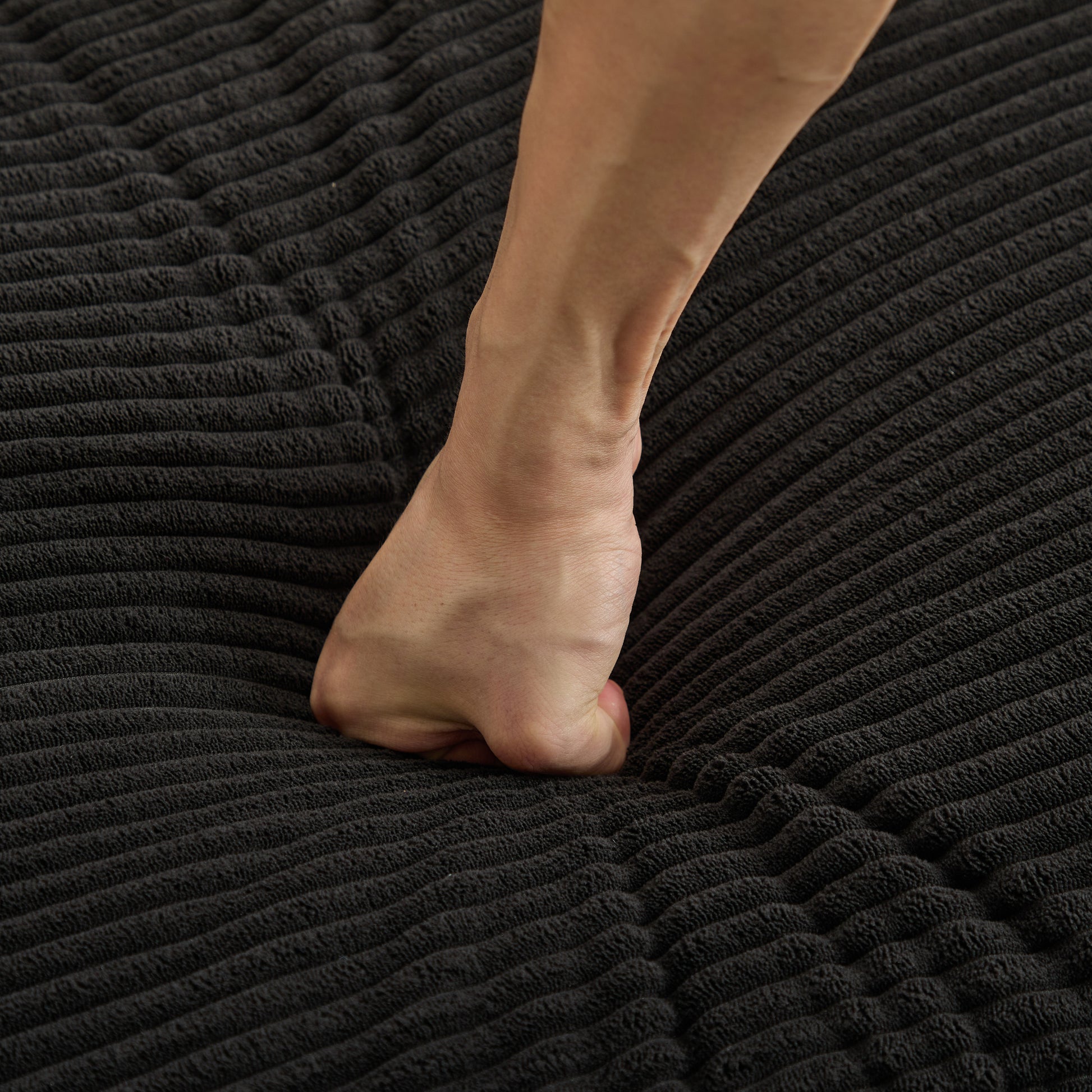 Closeup of hand pressing into soft dark grey corduroy fabric showing material density