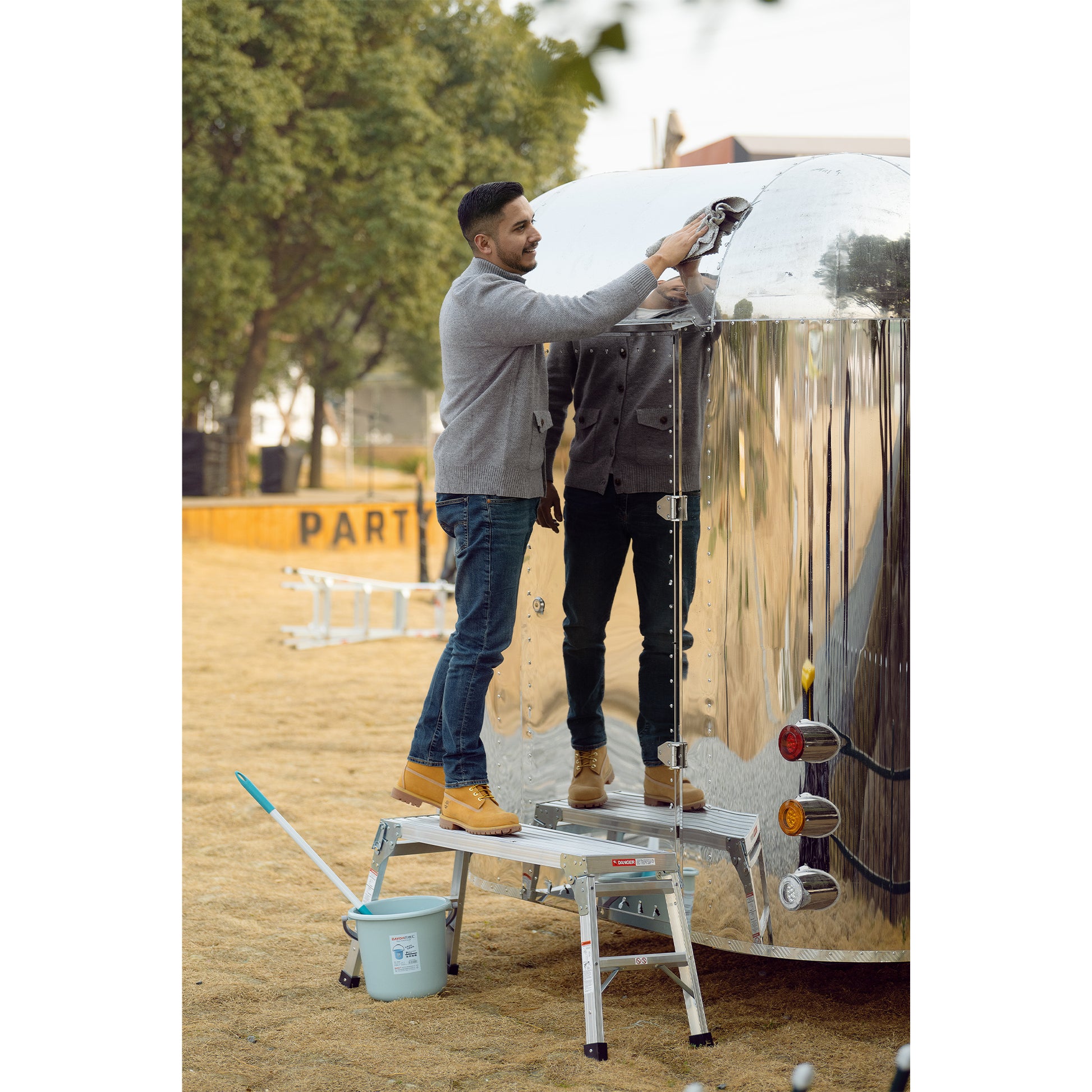 Man cleaning silver RV with microfiber cloth on a folding work platform