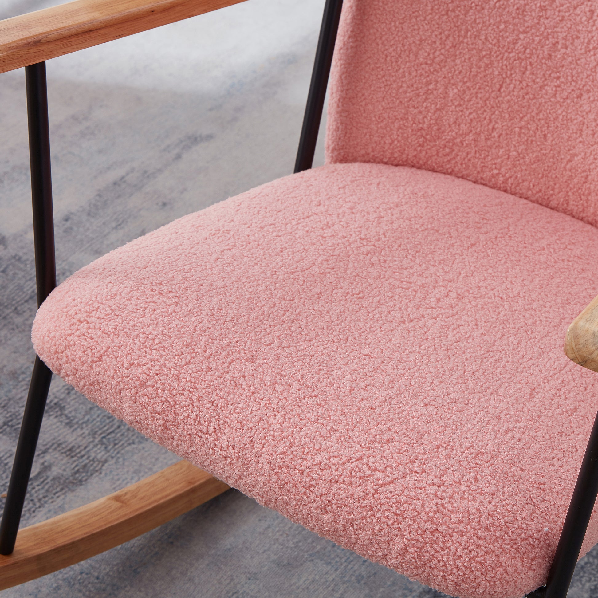 Close up of a plush pink sherpa fabric seat on a modern rocking chair with wooden armrests