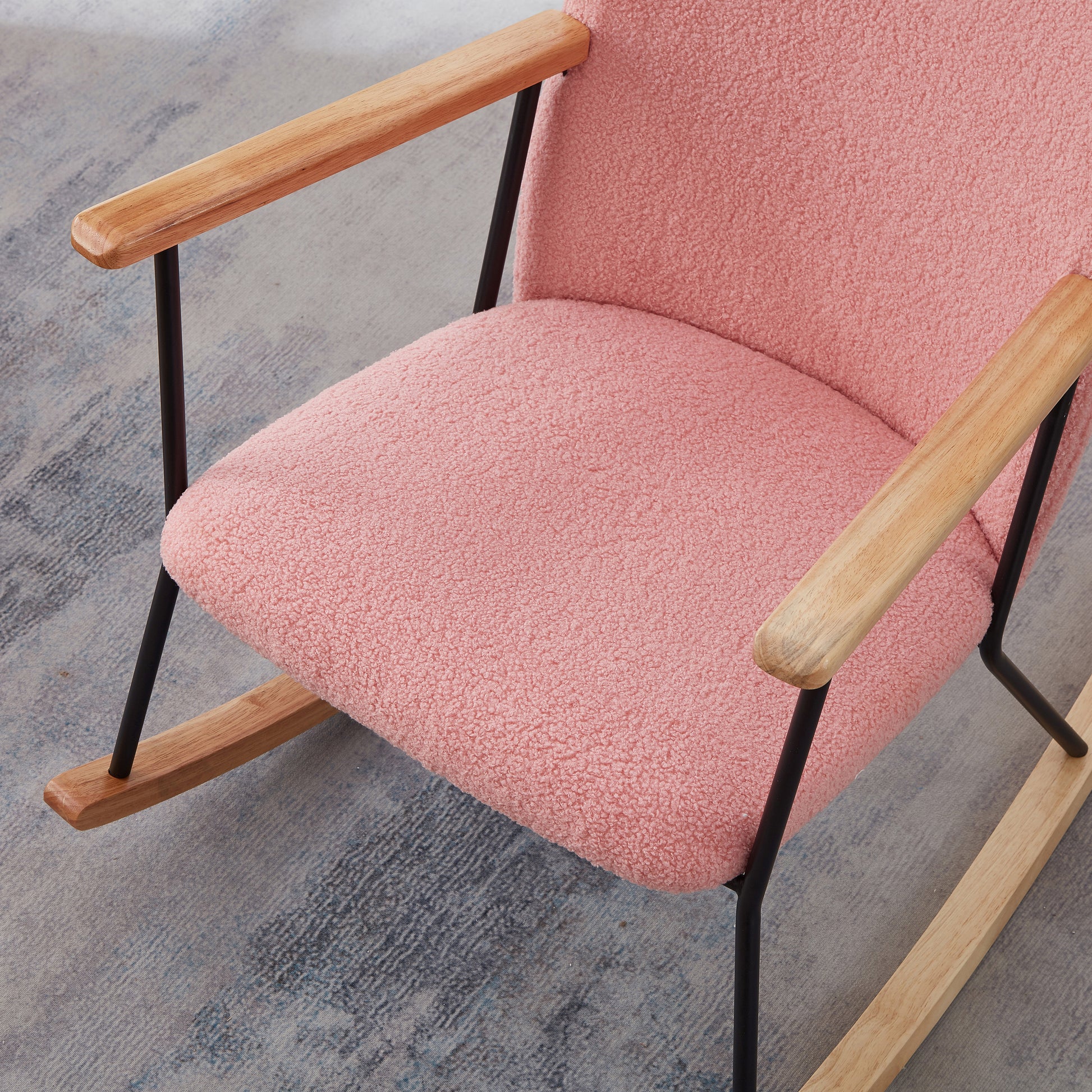 Pink boucle fabric rocking chair with natural wood armrests and black metal legs