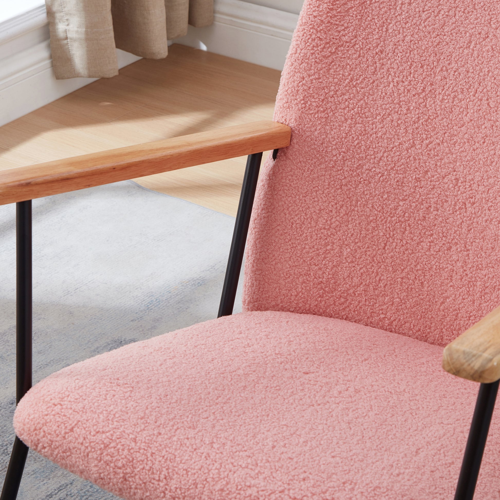 Closeup of a plush pink armchair with wooden armrests and black metal legs