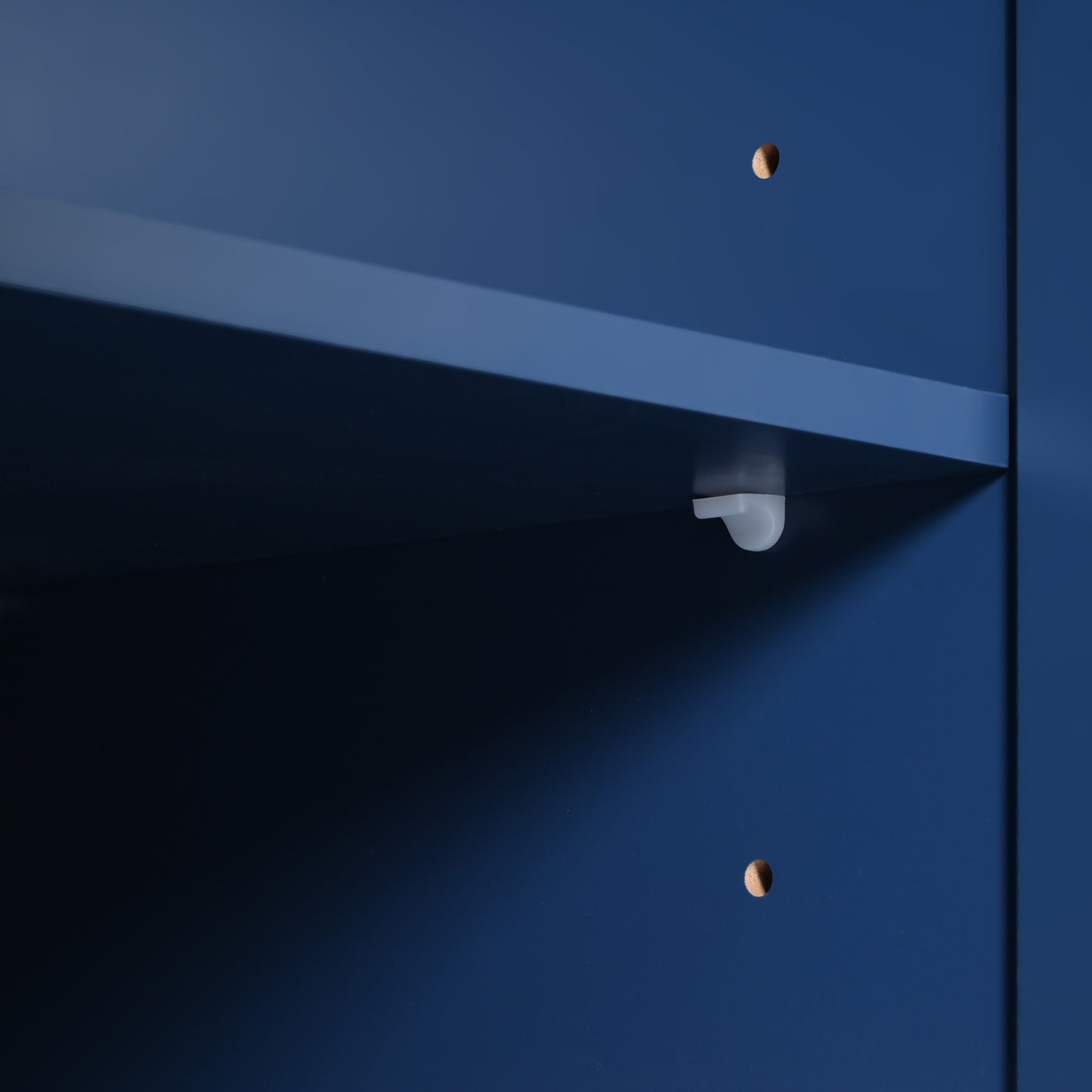 Closeup of a white plastic shelf support peg inside a dark blue cabinet