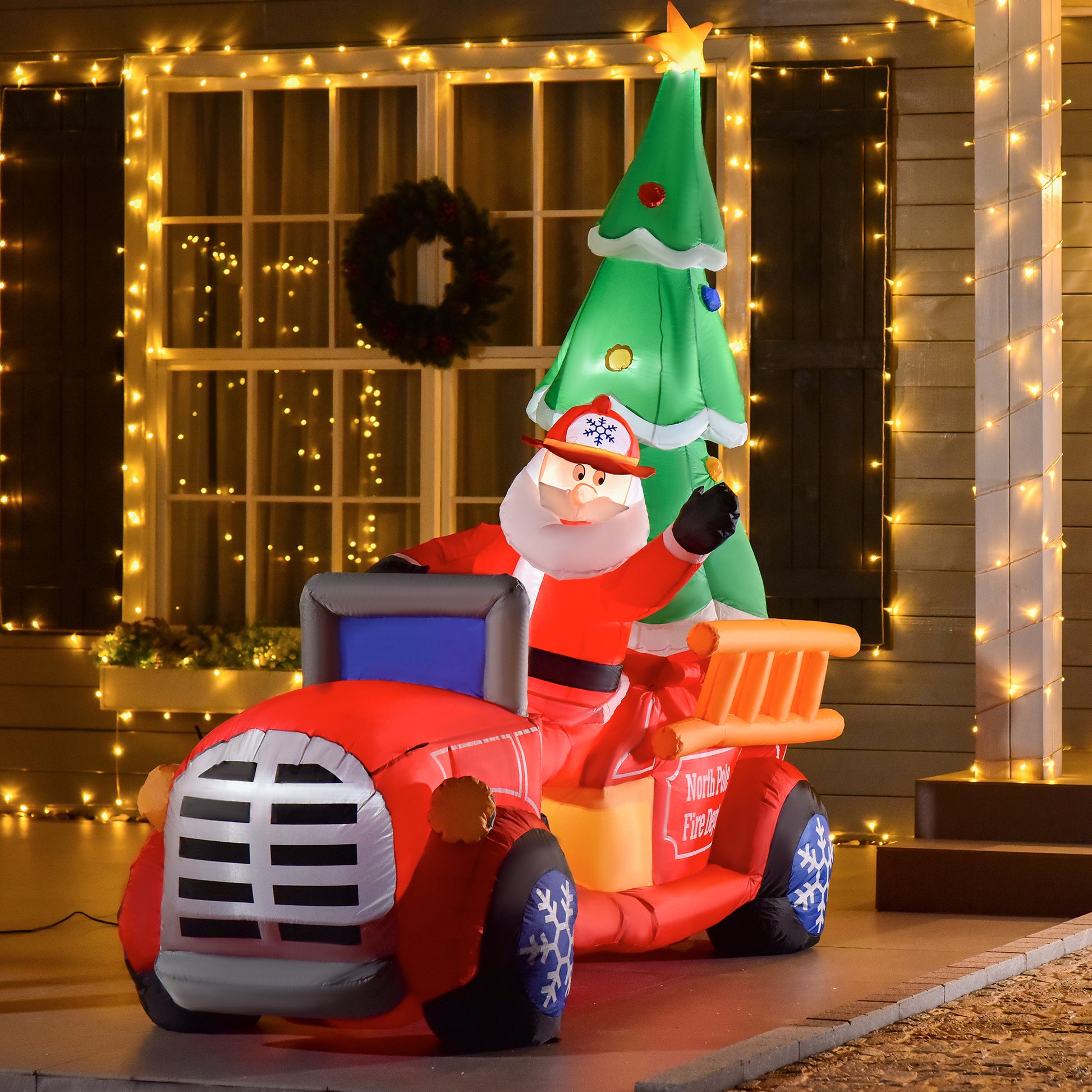 Inflatable Santa driving a red fire truck with a Christmas tree on the back