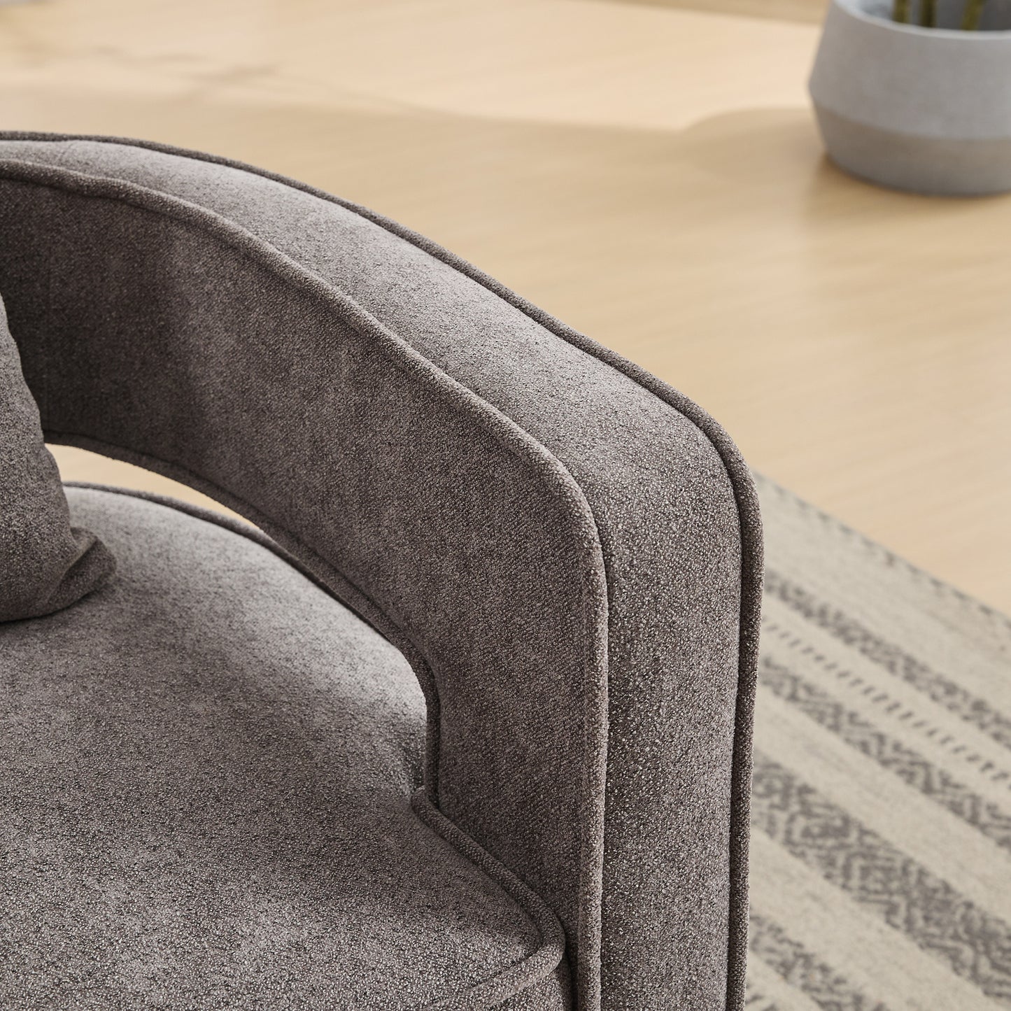 Closeup of a textured grey fabric accent chair with a curved armrest