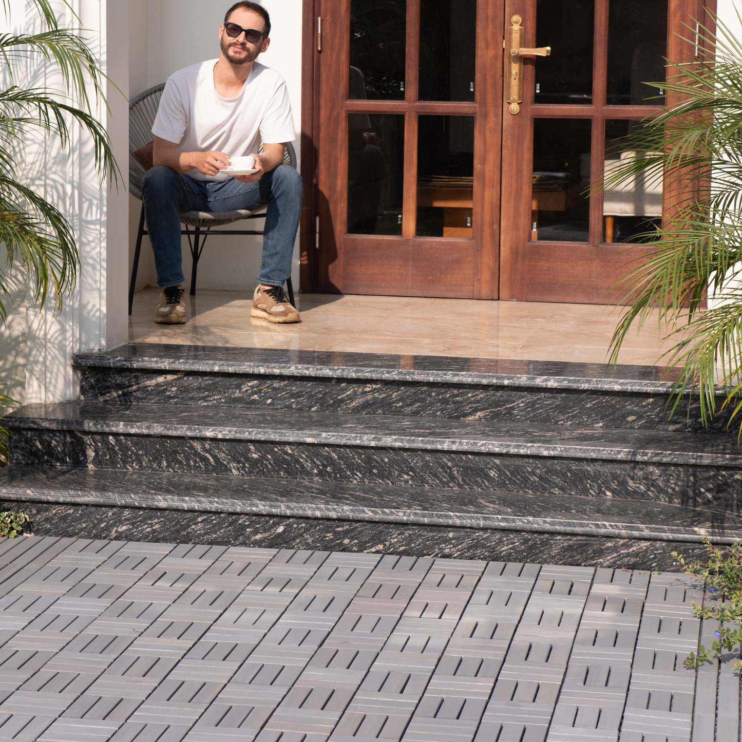 Man in white tshirt and blue jeans enjoys coffee on a patio chair near granite steps