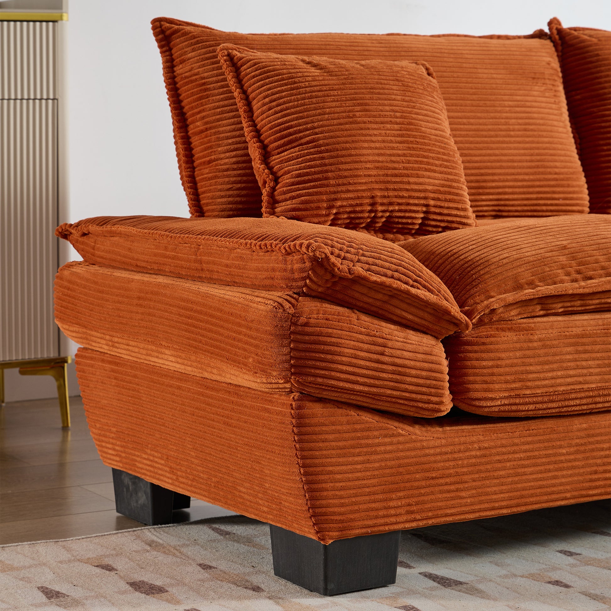 Closeup of plush orange corduroy sofa with textured cushions and dark block legs