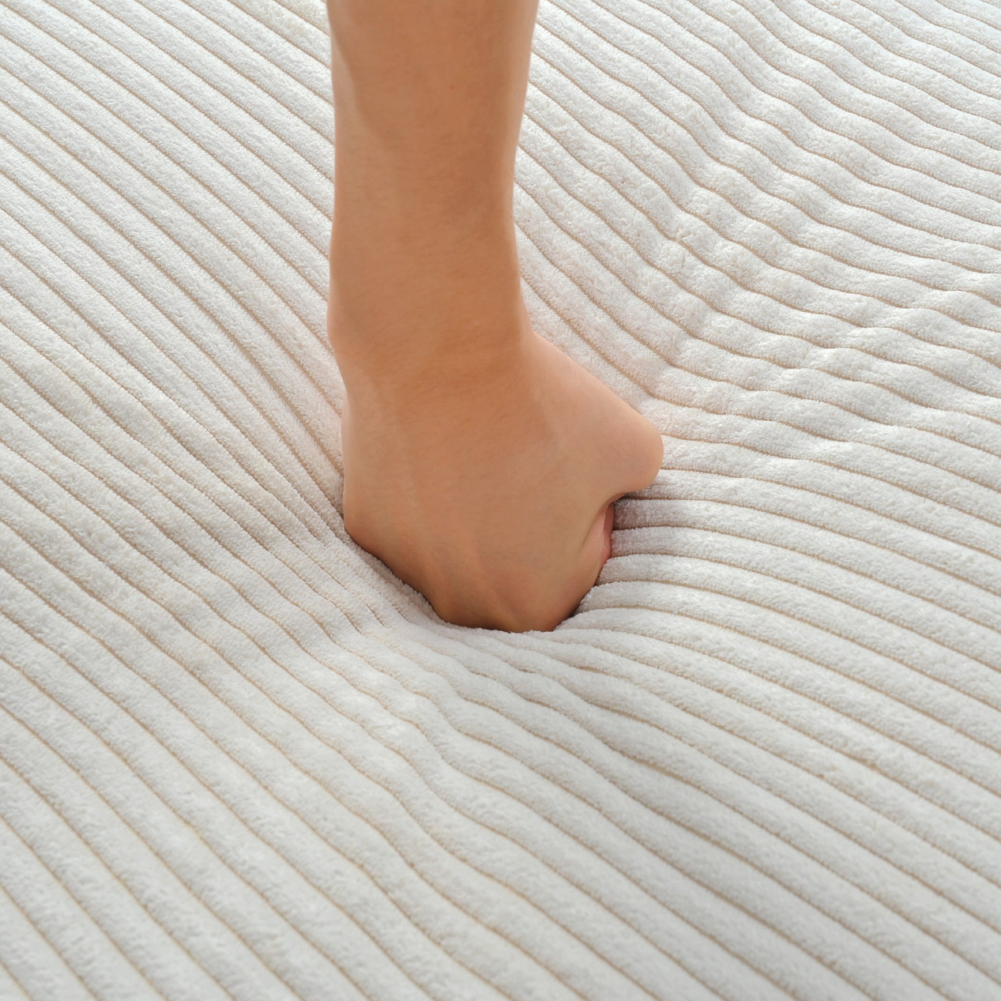 Closeup of a soft plush cream corduroy fabric with diagonal ridges showing foot indentation