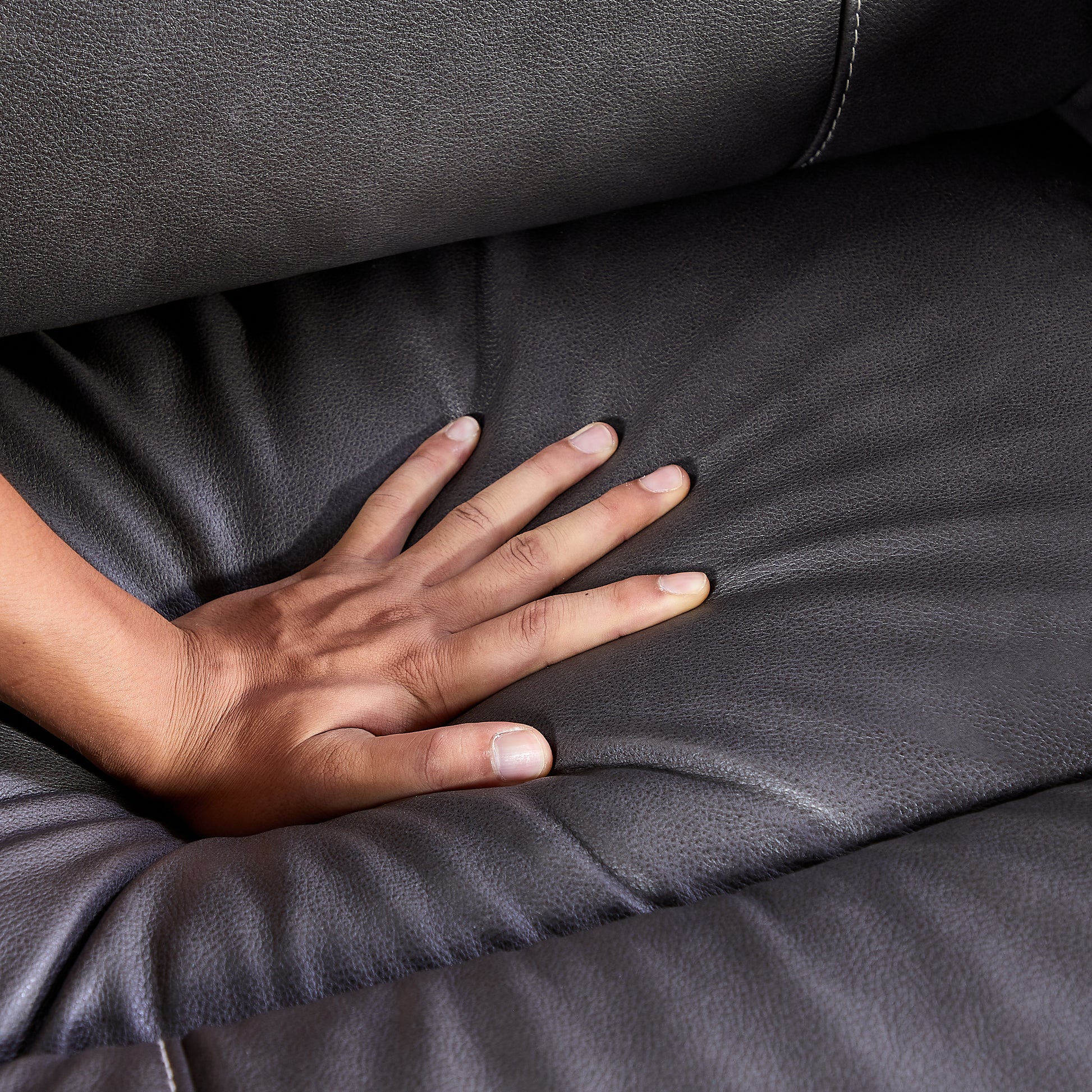 Closeup of a hand pressing into plush dark grey faux leather couch cushion for comfort