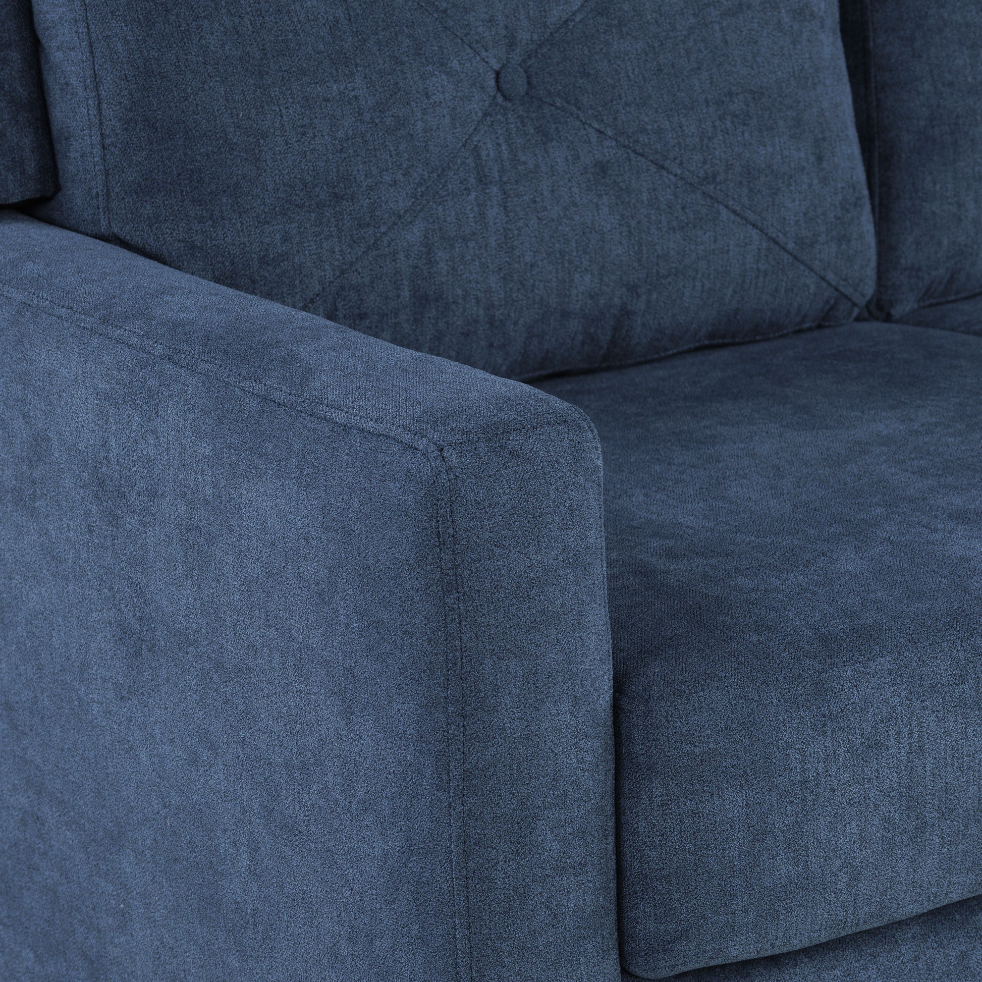 Closeup of a navy blue textured fabric sofa armrest and tufted cushion