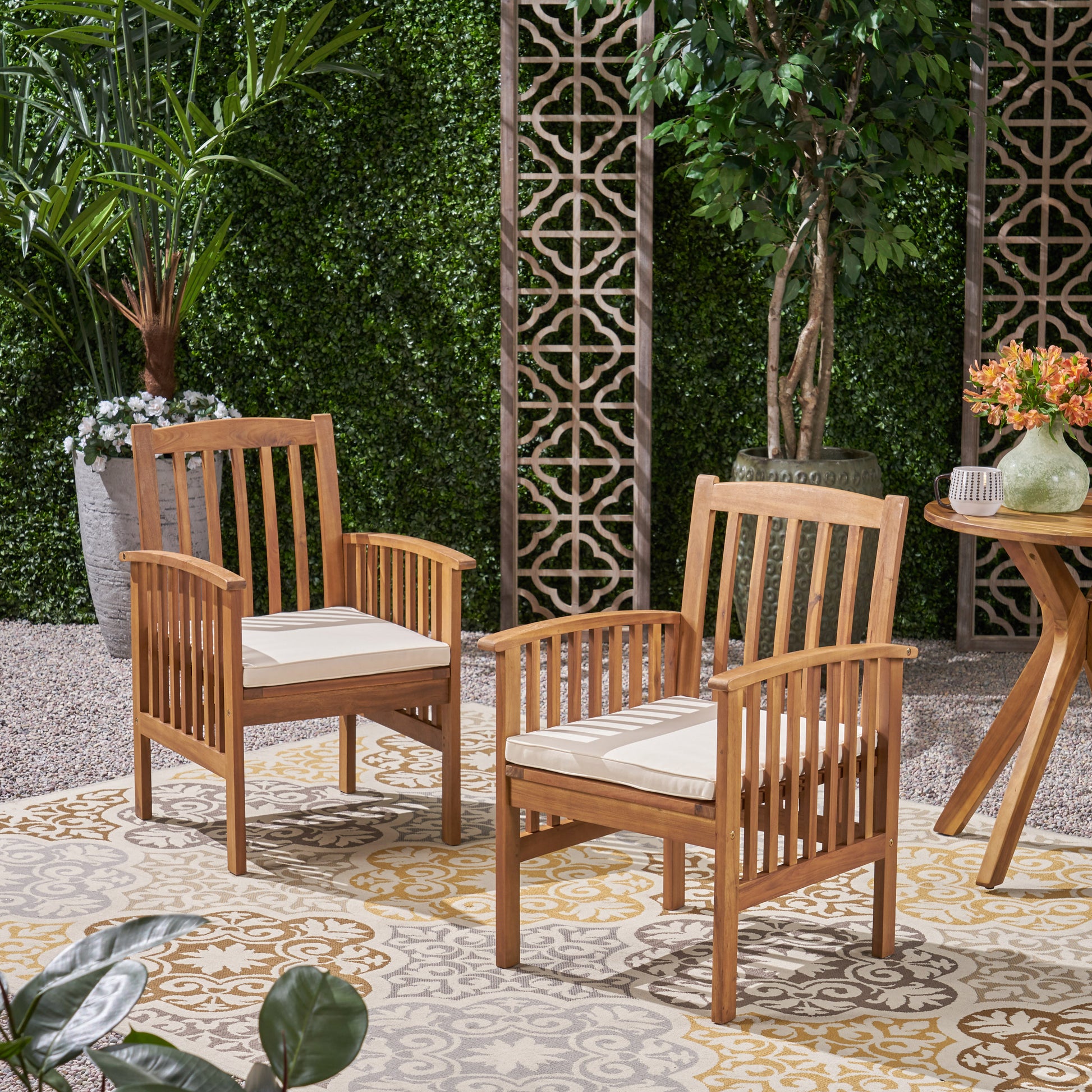 Two modern teak wood patio chairs with cream cushions offer comfortable outdoor seating