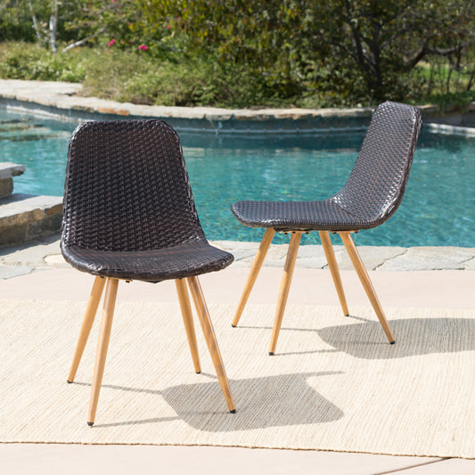 Dark brown wicker dining chairs with tapered wooden legs on a patio near a pool