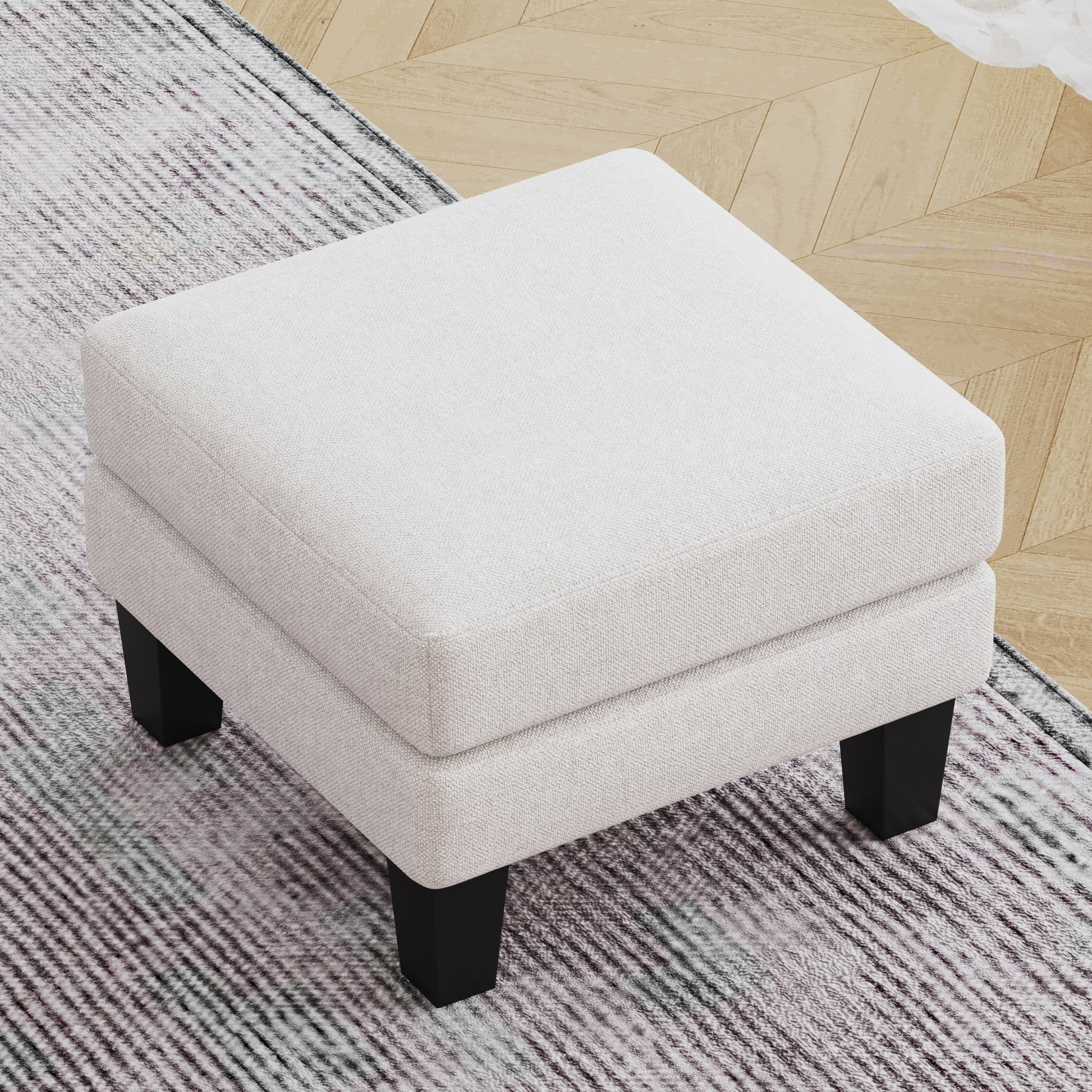 Cream linen upholstered square ottoman with black tapered legs on a patterned rug