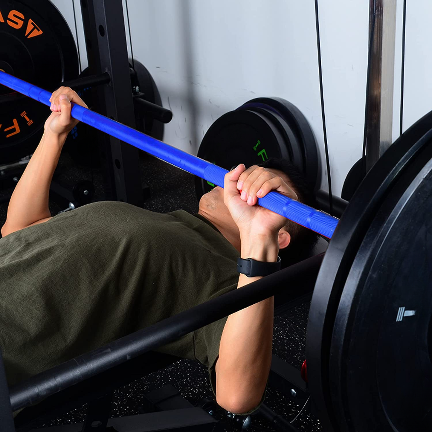 Man performing bench press with a blue barbell and weighted plates in a gym
