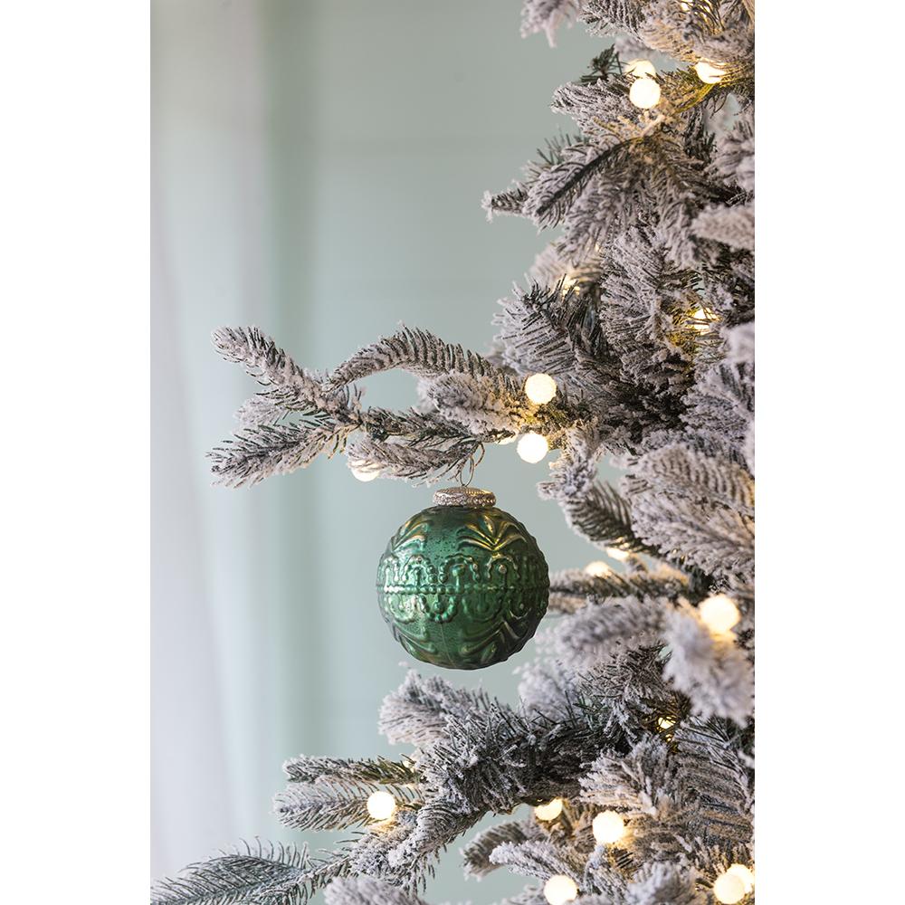 Green glass Christmas ornament with embossed floral pattern hanging on flocked tree branch