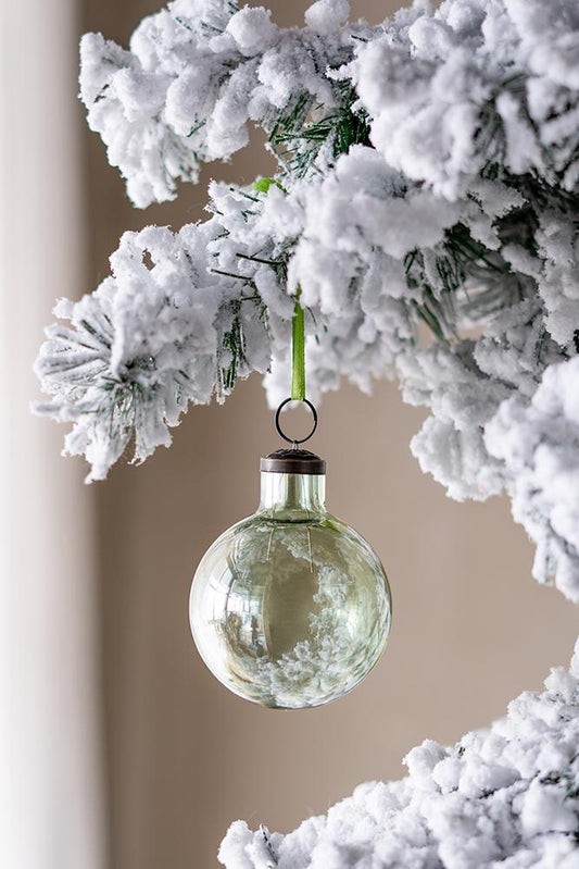 Frosted glass Christmas ornament with a subtle green tint hanging from a snowdusted branch