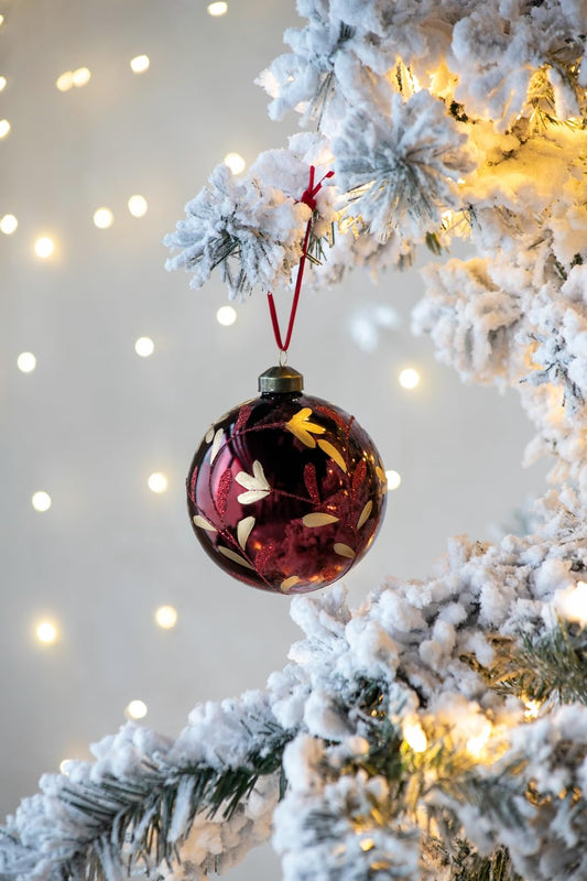 Deep red glass Christmas ornament with gold floral pattern hanging on flocked tree