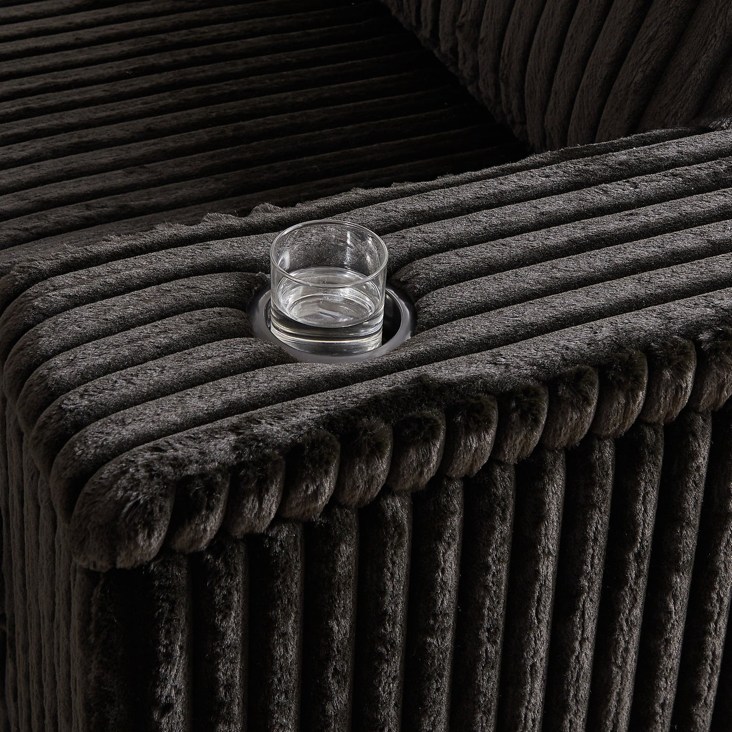 Dark grey corduroy sofa armrest with integrated cup holder and glass