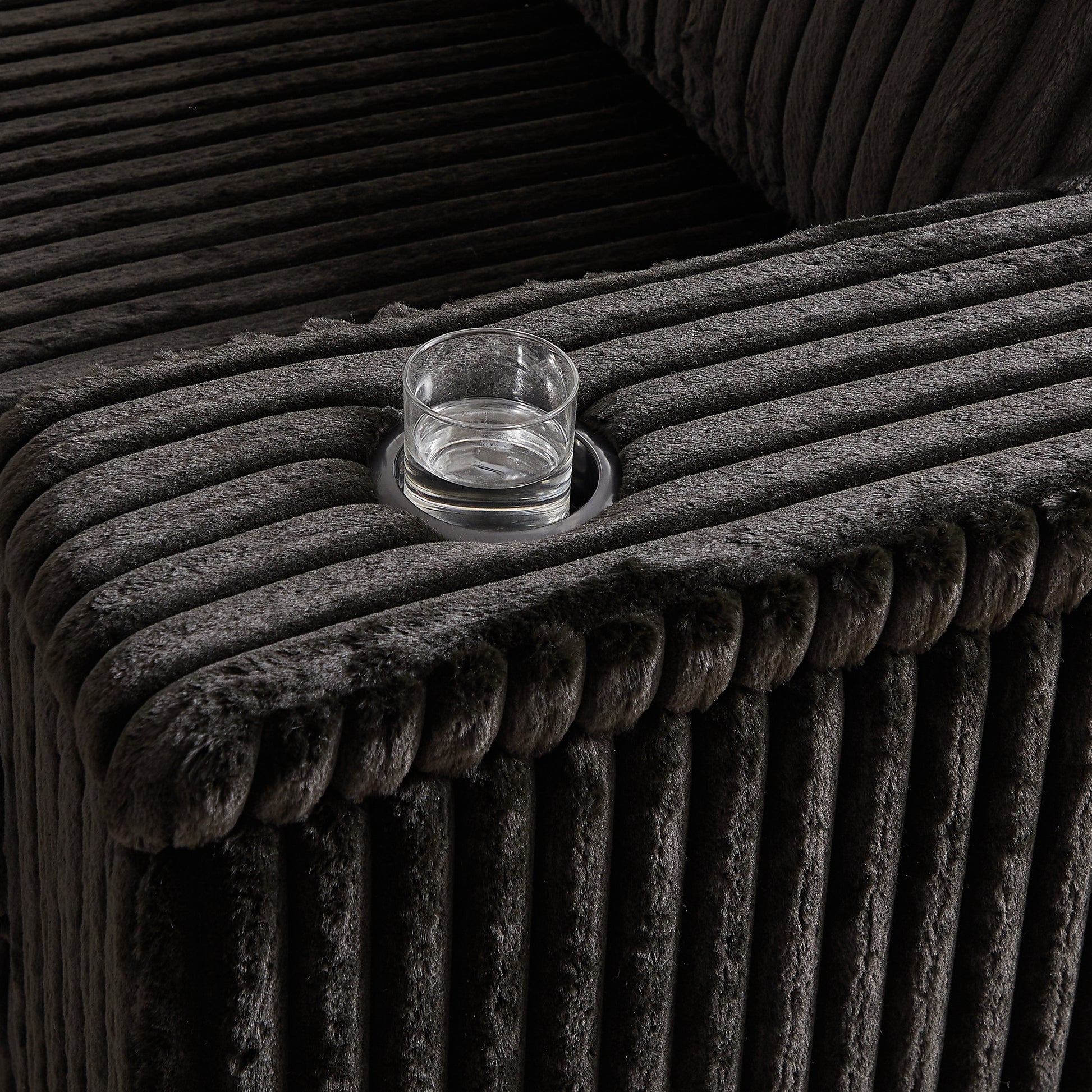 Dark grey corduroy sofa armrest with integrated cup holder and glass