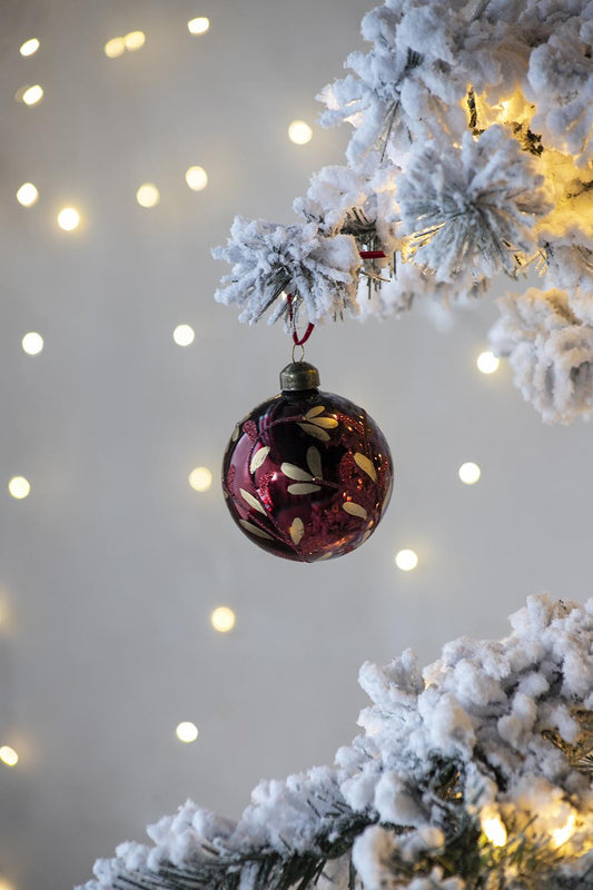 Burgundy glass Christmas ornament with gold leaf pattern hanging on a flocked tree branch