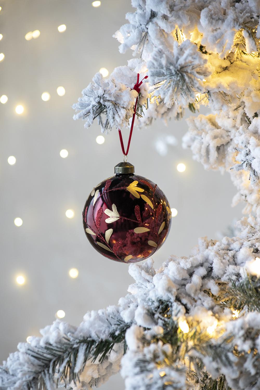 Deep red glass Christmas ornament with gold leaf pattern hanging on flocked tree