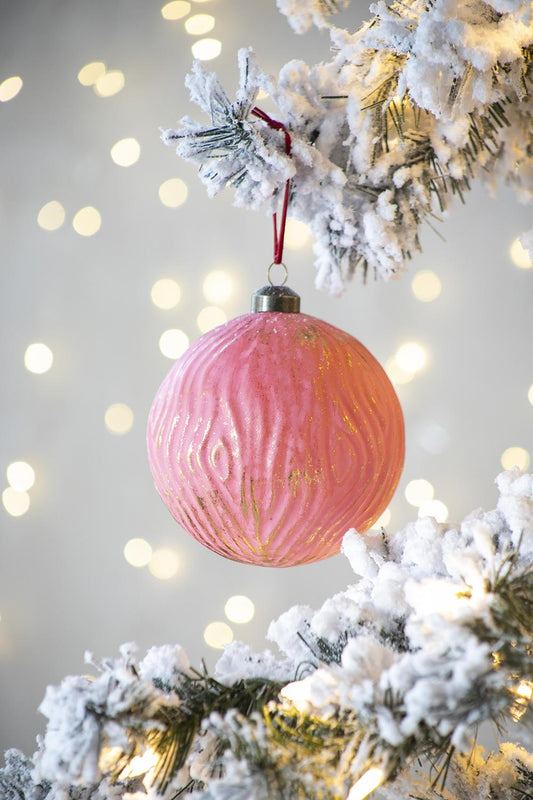 Pink glass Christmas ornament with gold swirling texture hanging on a flocked tree branch