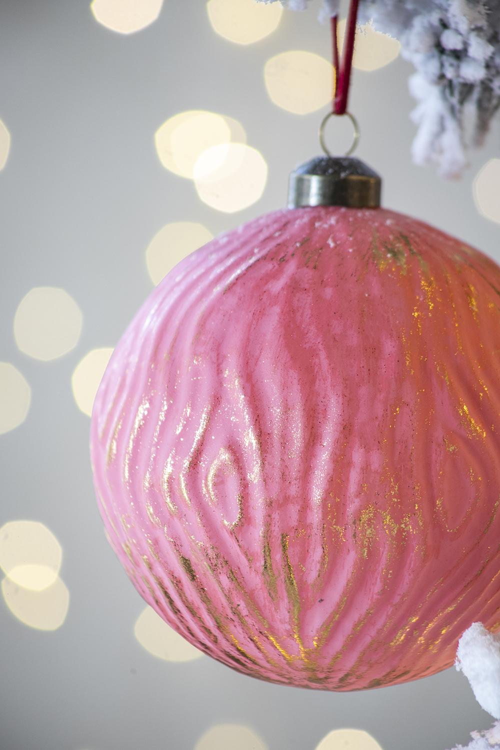 Textured pink glass Christmas ornament with gold accents hanging on a tree