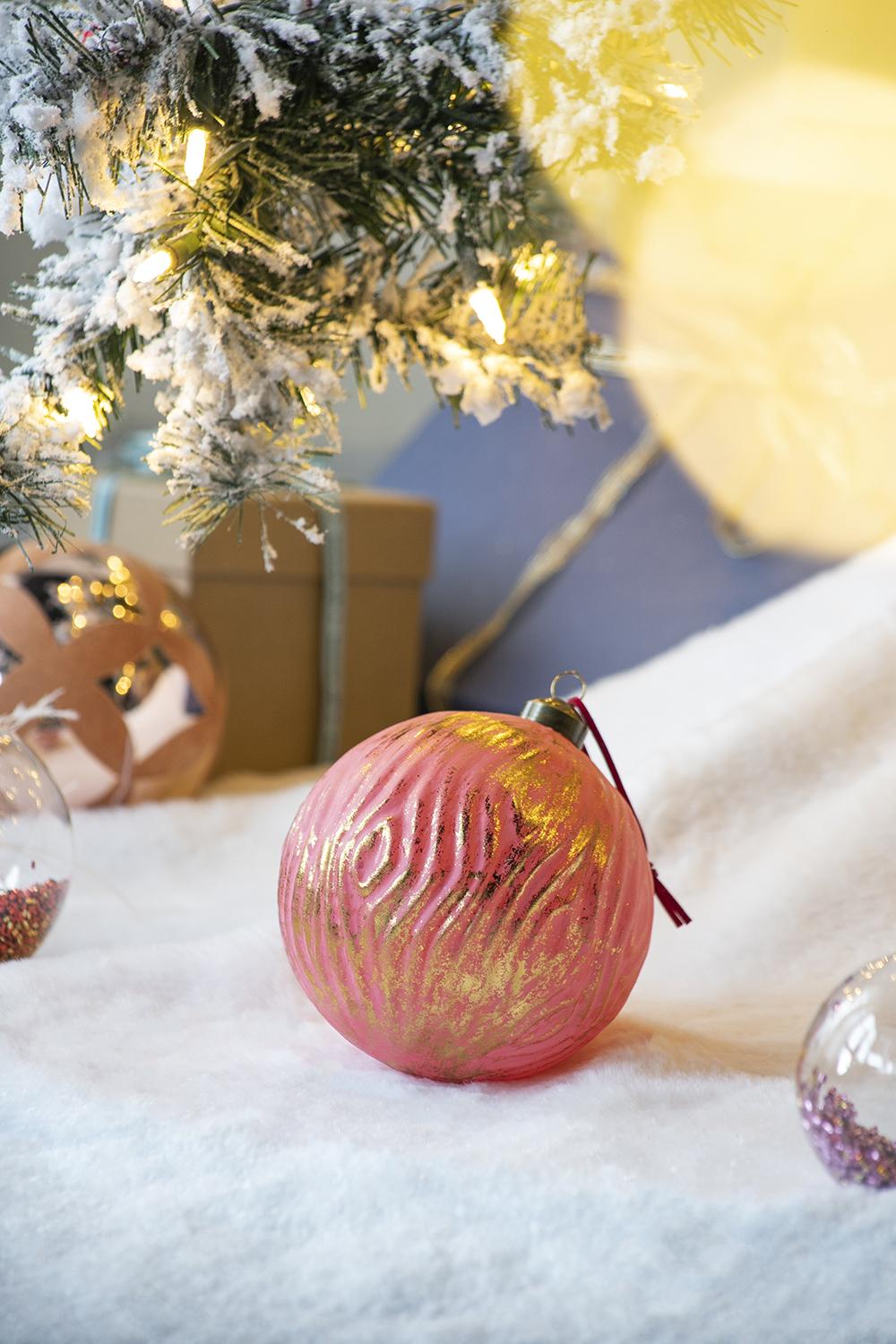 Textured pink glass Christmas ornament with gold accents on flocked tree branch