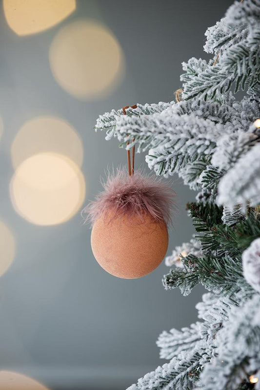 Peachcolored Christmas ornament with fuzzy trim hanging on a frosted tree branch